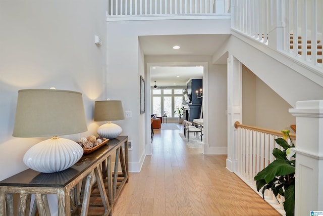 corridor featuring recessed lighting, light wood-type flooring, baseboards, and a high ceiling