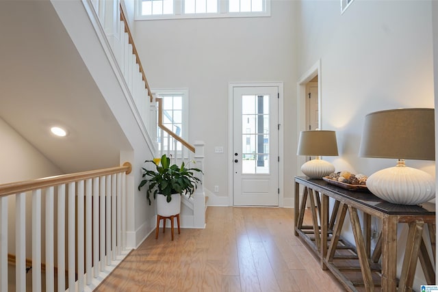 foyer entrance with stairs, baseboards, light wood-type flooring, and a towering ceiling