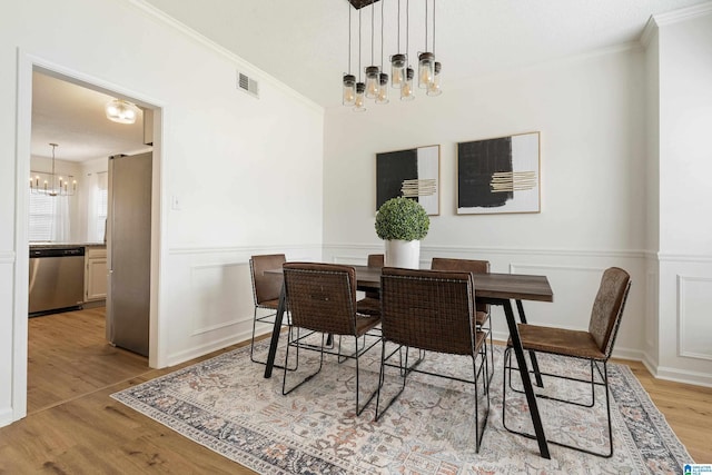 dining room featuring wood finished floors, a wainscoted wall, visible vents, crown molding, and a chandelier