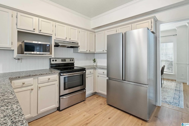 kitchen featuring under cabinet range hood, ornamental molding, light stone counters, appliances with stainless steel finishes, and light wood-style floors