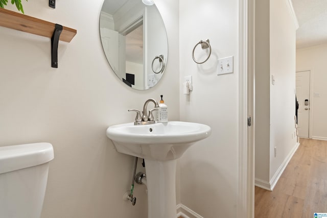 half bathroom with toilet, wood finished floors, baseboards, and ornamental molding