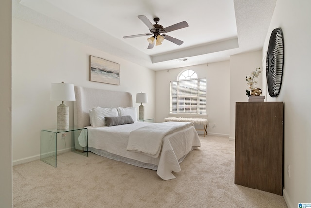 bedroom with visible vents, baseboards, ceiling fan, light carpet, and a raised ceiling