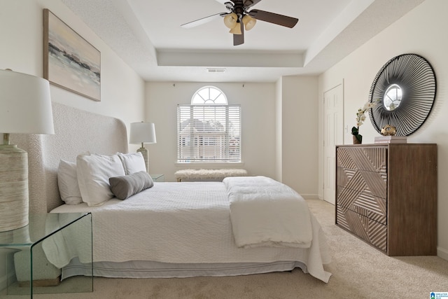 bedroom featuring visible vents, light carpet, a tray ceiling, baseboards, and ceiling fan