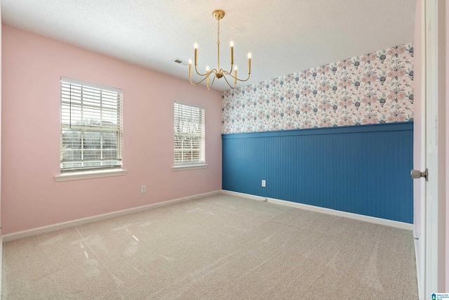 unfurnished room with wallpapered walls, a wainscoted wall, carpet floors, a notable chandelier, and a textured ceiling