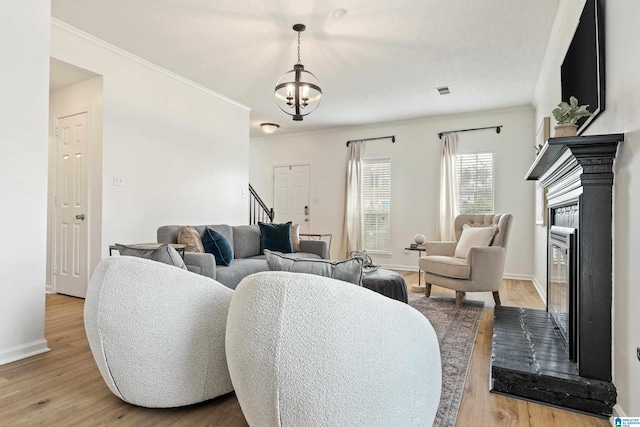 living area featuring stairway, baseboards, light wood-style floors, and a glass covered fireplace