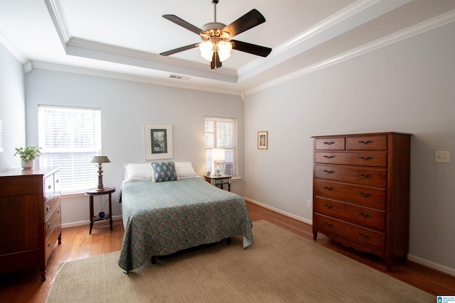 bedroom with light wood-type flooring, visible vents, ornamental molding, baseboards, and a raised ceiling