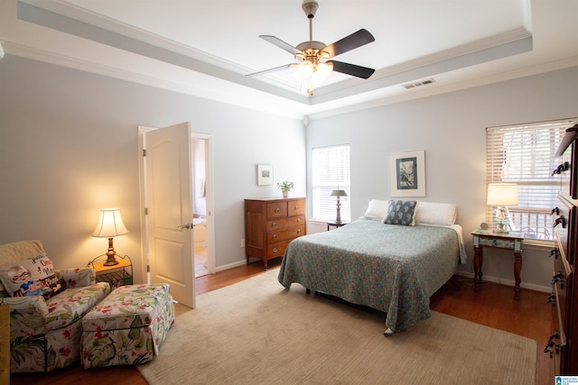 bedroom featuring baseboards, visible vents, ornamental molding, a raised ceiling, and light wood-type flooring