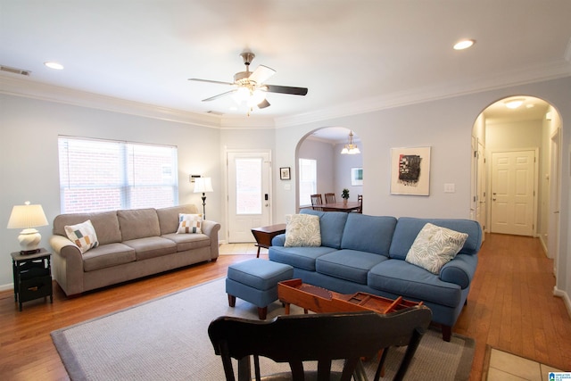 living area featuring light wood-type flooring, visible vents, ornamental molding, a ceiling fan, and arched walkways