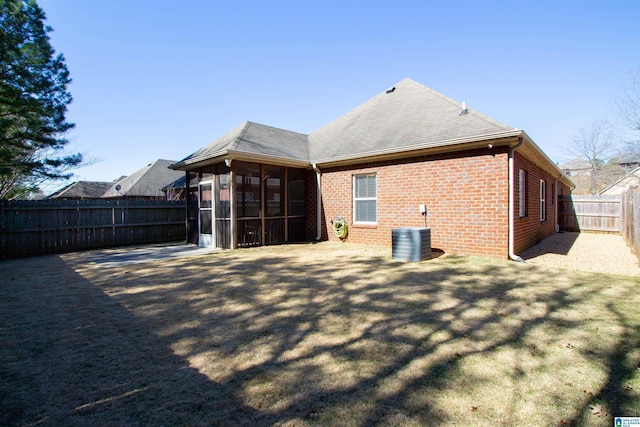 rear view of house featuring brick siding, central air condition unit, a lawn, a fenced backyard, and a sunroom