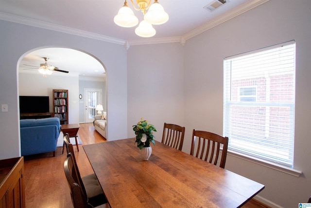 dining space with visible vents, light wood-style flooring, arched walkways, crown molding, and a wealth of natural light