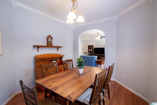 dining space featuring arched walkways, crown molding, baseboards, and wood finished floors