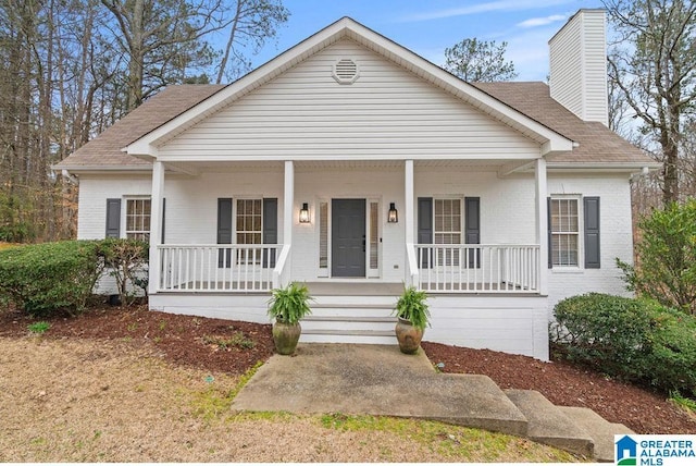 bungalow-style house featuring brick siding, covered porch, and roof with shingles