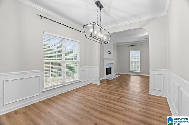 unfurnished living room featuring a premium fireplace, ornamental molding, wainscoting, an inviting chandelier, and wood finished floors