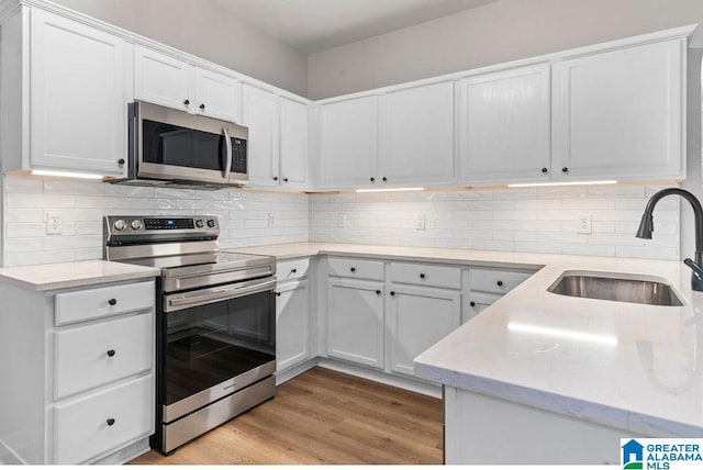 kitchen featuring tasteful backsplash, light wood-style flooring, white cabinets, stainless steel appliances, and a sink