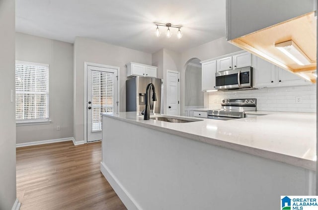 kitchen with backsplash, wood finished floors, arched walkways, stainless steel appliances, and a sink