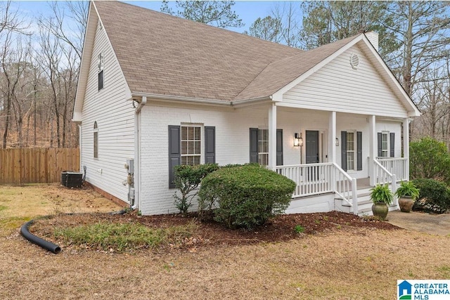 view of front facade with central AC unit, fence, a porch, a shingled roof, and brick siding