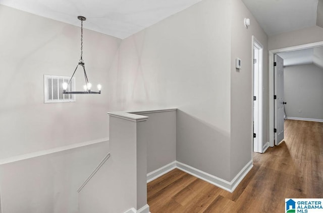 corridor with wood finished floors, visible vents, an upstairs landing, and a chandelier