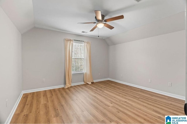 spare room featuring visible vents, a ceiling fan, light wood finished floors, baseboards, and vaulted ceiling