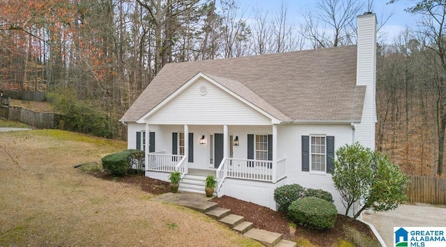 view of front facade with a porch, fence, roof with shingles, a front yard, and a chimney