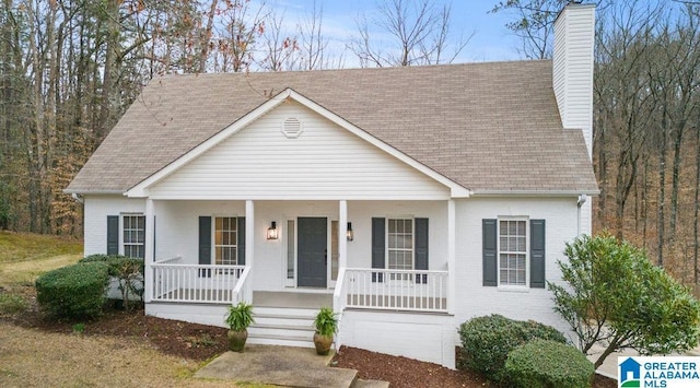 view of front of house with brick siding, a porch, a chimney, and roof with shingles