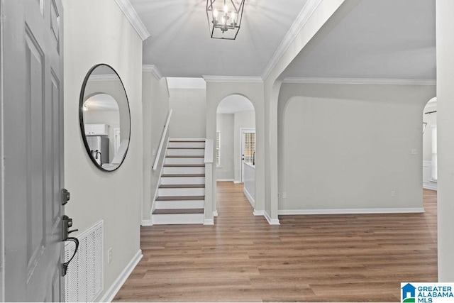 entrance foyer featuring visible vents, baseboards, ornamental molding, wood finished floors, and arched walkways