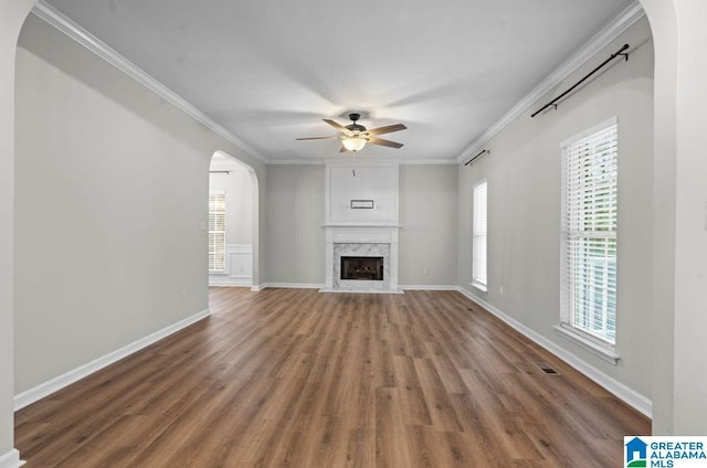 unfurnished living room with baseboards, ceiling fan, ornamental molding, wood finished floors, and arched walkways