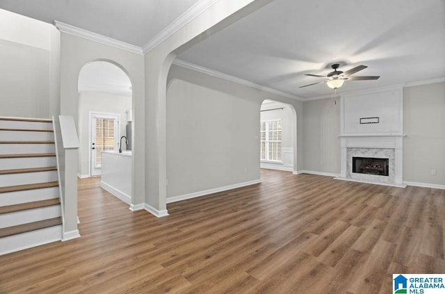 unfurnished living room featuring ornamental molding, wood finished floors, arched walkways, and ceiling fan