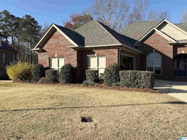 view of front facade featuring brick siding, a front lawn, and a shingled roof