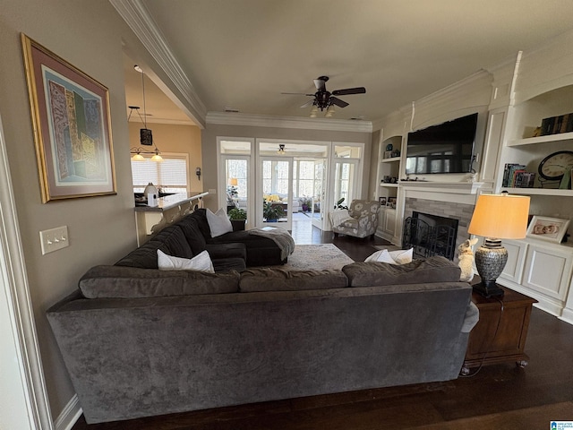 living area featuring wood finished floors, a fireplace, a ceiling fan, and crown molding