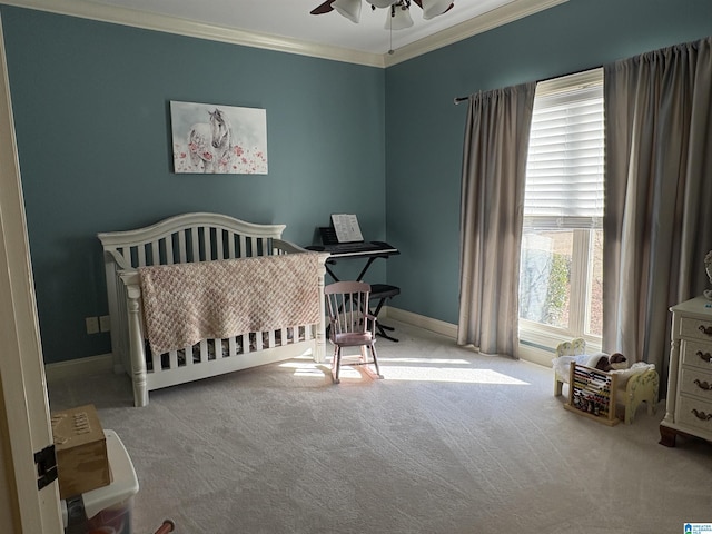 bedroom featuring a crib, carpet floors, crown molding, baseboards, and ceiling fan