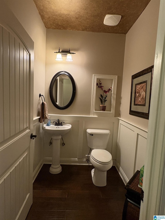 bathroom with wood finished floors, wainscoting, a textured ceiling, a decorative wall, and toilet