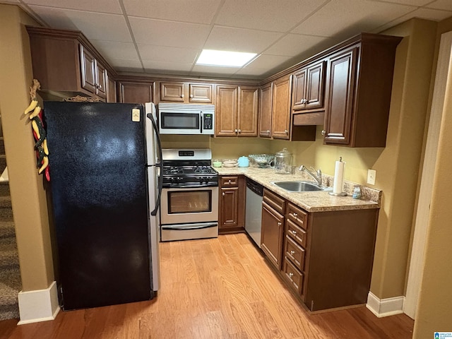 kitchen featuring light wood-style flooring, a sink, stainless steel appliances, light countertops, and a paneled ceiling