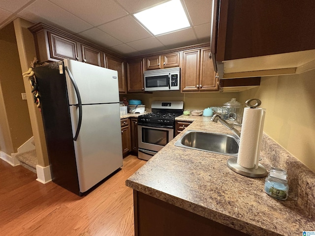 kitchen featuring a drop ceiling, a sink, dark brown cabinets, light wood-style floors, and appliances with stainless steel finishes