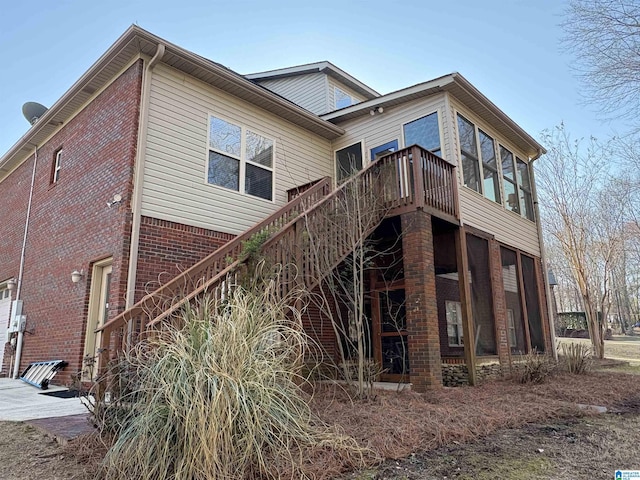 view of side of property with a deck, stairway, brick siding, and a sunroom