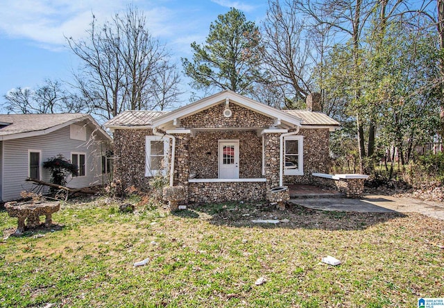 view of front facade with stone siding, a patio, a chimney, and a front yard