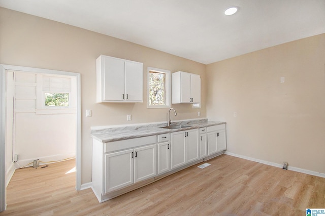 kitchen with light wood-type flooring, a sink, white cabinets, baseboards, and light stone countertops