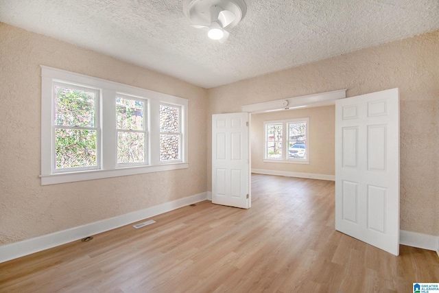 spare room with visible vents, baseboards, light wood-style floors, a textured wall, and a textured ceiling