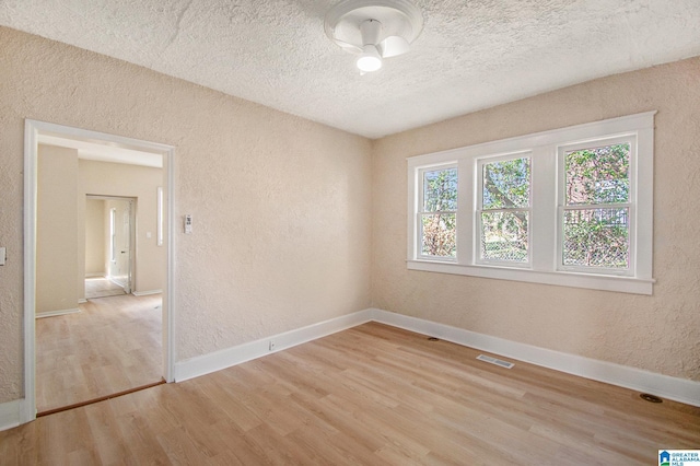 empty room featuring baseboards, visible vents, light wood finished floors, a textured ceiling, and a textured wall