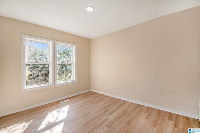 spare room with light wood-type flooring, visible vents, and baseboards