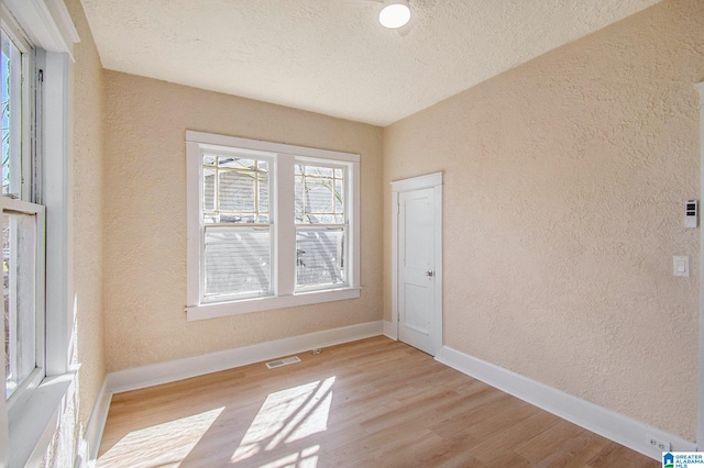 empty room featuring visible vents, baseboards, light wood-style floors, a textured wall, and a textured ceiling