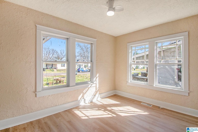 unfurnished room featuring wood finished floors, a textured wall, baseboards, and a wealth of natural light