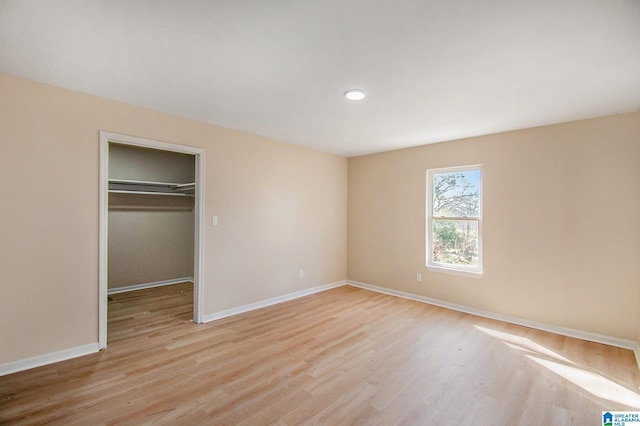 unfurnished bedroom featuring a walk in closet, a closet, baseboards, and light wood finished floors