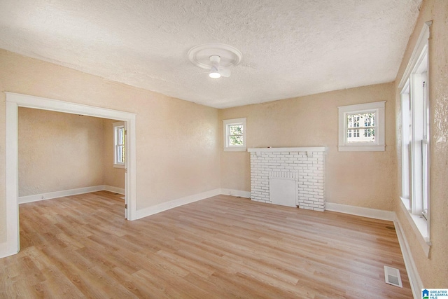 unfurnished room featuring baseboards, visible vents, light wood-style flooring, a fireplace, and a textured ceiling