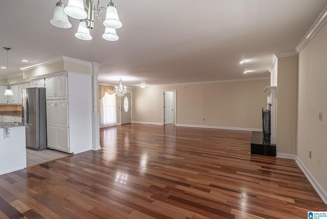 unfurnished living room with an inviting chandelier, crown molding, and wood finished floors