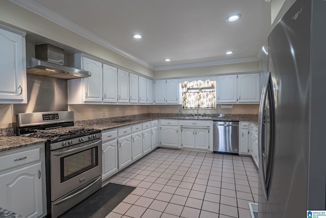 kitchen with wall chimney range hood, ornamental molding, appliances with stainless steel finishes, light tile patterned flooring, and white cabinets