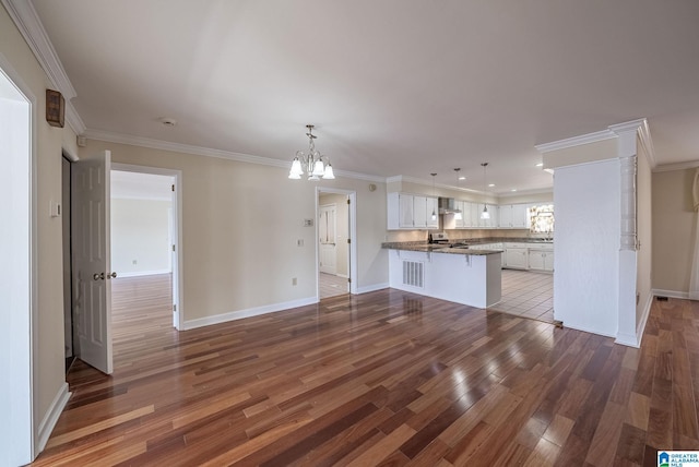 unfurnished living room with a notable chandelier, crown molding, baseboards, and wood finished floors