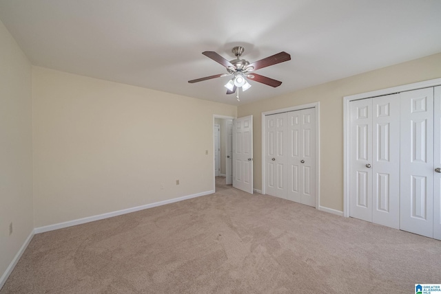 unfurnished bedroom with two closets, a ceiling fan, baseboards, and carpet floors