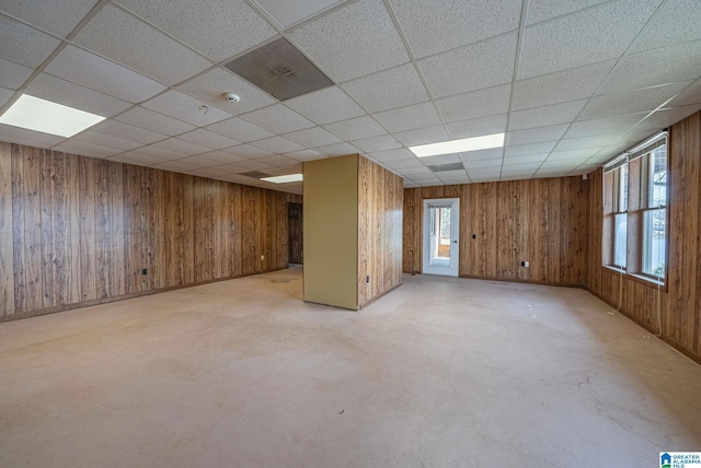 unfurnished room with wooden walls, a paneled ceiling, and concrete floors