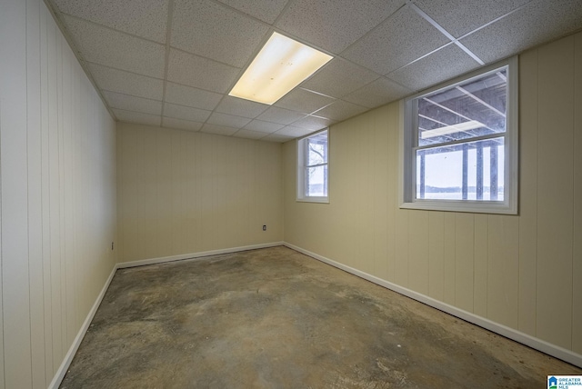 basement featuring a wealth of natural light, a drop ceiling, wood walls, and baseboards