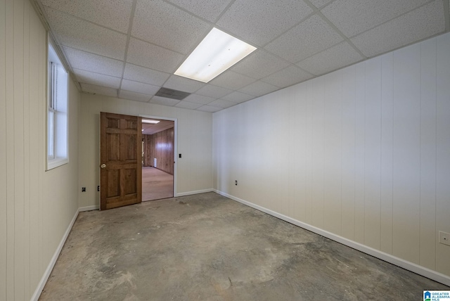 unfurnished room with a drop ceiling, unfinished concrete floors, and baseboards